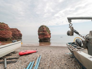 A pebble beach with boats and a red paddleboard near rock formations by the sea at The Retreat in Otterton