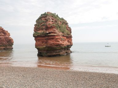 A large rock formation in the water near a pebble beach with a small boat in the distance at The Retreat in Otterton