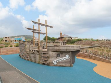 An outdoor playground with a wooden pirate ship structure on blue and yellow rubber flooring at The Retreat in Otterton