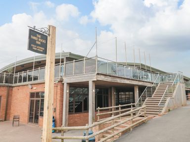 An exterior view of a two story building with a wooden sign reading The Three Rocks Inn and stairs leading to a balcony at The Retreat in Otterton