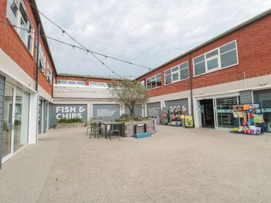 An outdoor courtyard with tables, chairs, string lights, and shops including a fish and chips outlet at The Retreat in Otterton
