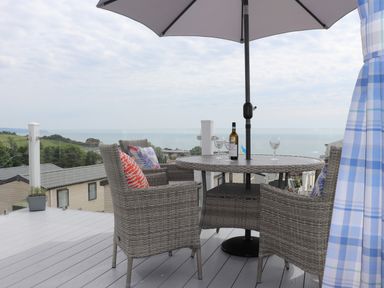 An outdoor deck with a round table and four chairs under an umbrella overlooking the sea at The Retreat in Otterton