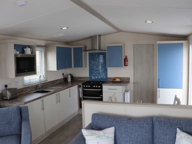 A kitchen with blue and white cabinets a stove and a sink next to a blue sofa at The Retreat in Otterton