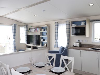A kitchen and dining area with a table set for four and a living room with a TV and blue armchair at The Retreat in Otterton
