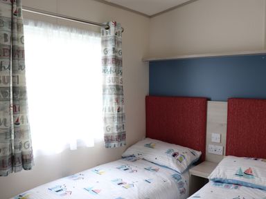 A bedroom with two single beds and a window with patterned curtains at The Retreat in Otterton