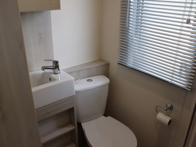 A small bathroom with a toilet a sink with a faucet a window with blinds and a toilet paper holder at The Retreat in Otterton