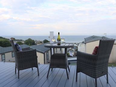 A balcony with a round table set with a bottle and two wine glasses and two chairs overlooking a residential area and the sea at The Retreat in Otterton