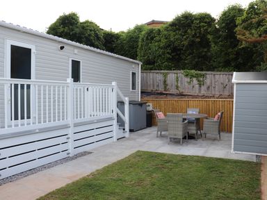 An outdoor patio area with a white railing, a grass lawn, a grey shed, and a table with four chairs at The Retreat in Otterton