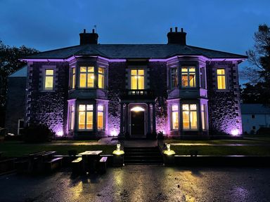A stone building with illuminated windows and purple lights outside at The Lloyd George in Bontnewydd Gwynedd