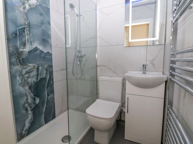 A bathroom with a shower, toilet, sink with cabinet, mirror, and towel radiator at The Lloyd George in Bontnewydd Gwynedd