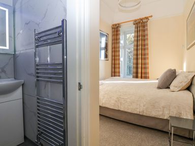 A bedroom with a bed and window with curtains beside a bathroom with a sink and towel radiator at The Lloyd George in Bontnewydd Gwynedd