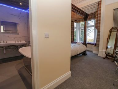 A bedroom with a four poster bed and a standing mirror next to a bathroom with a bathtub and a sink at The Lloyd George in Bontnewydd Gwynedd