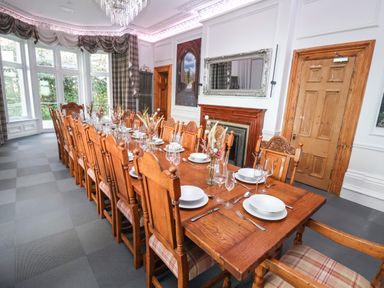 A dining room with a long wooden table set with plates glasses and cutlery surrounded by wooden chairs at The Lloyd George in Bontnewydd Gwynedd