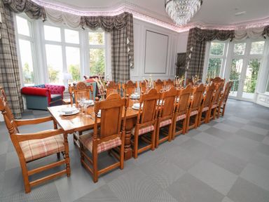 A large dining room with a long wooden table set with plates and glasses and wooden chairs with plaid cushions at The Lloyd George in Bontnewydd Gwynedd