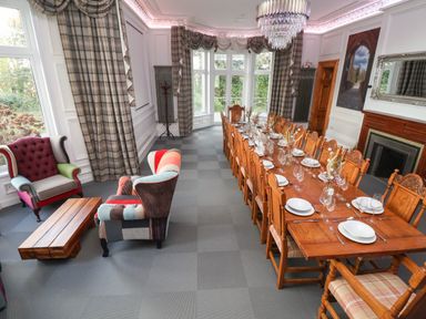 A dining room with a long wooden table and multiple chairs and two armchairs with a wooden coffee table at The Lloyd George in Bontnewydd Gwynedd
