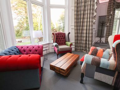 A sitting area with multicolored armchairs a wooden coffee table and large windows at The Lloyd George in Bontnewydd Gwynedd