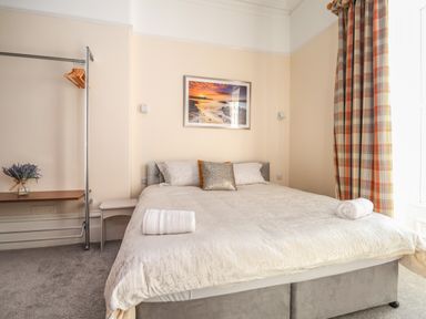 A bedroom with a double bed two rolled towels a clothing rack and checked curtains at The Lloyd George in Bontnewydd Gwynedd