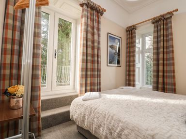 A bedroom with a bed, plaid curtains, a framed picture on the wall, and a small table with flowers at The Lloyd George in Bontnewydd, Gwynedd