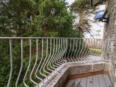 A balcony with metal railing overlooking trees and a stone wall at The Lloyd George in Bontnewydd Gwynedd