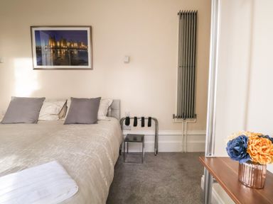 A bedroom with a bed two gray pillows a wall heater a framed picture and a table with flowers at The Lloyd George in Bontnewydd Gwynedd