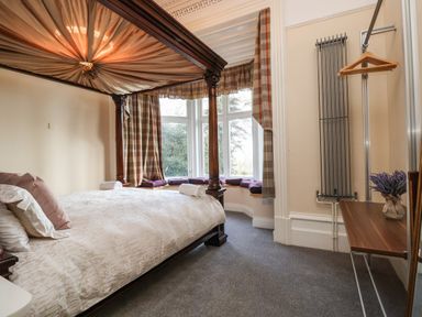 A bedroom with a four-poster bed and bay window seating with cushions at The Lloyd George in Bontnewydd Gwynedd