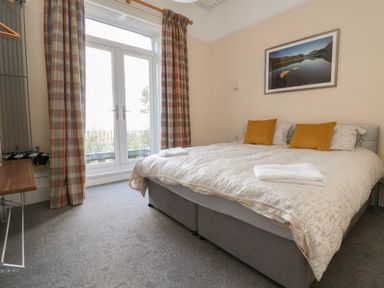 A bedroom with a double bed with orange cushions and folded towels near large windows with plaid curtains at The Lloyd George in Bontnewydd Gwynedd