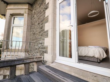 An open door leading to a bedroom with a bed inside on a stone and brick exterior balcony at The Lloyd George in Bontnewydd Gwynedd