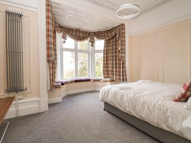 A bedroom with a bed next to a bay window with plaid curtains and cushions at The Lloyd George in Bontnewydd Gwynedd