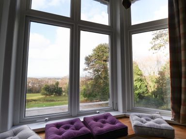 A bay window with three cushions on the wooden seat overlooking trees and a field at The Lloyd George in Bontnewydd Gwynedd