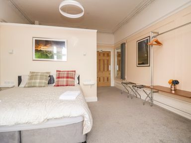 A bedroom with a double bed and plaid cushions a wooden door and a wall-mounted clothes rack with hangers at The Lloyd George in Bontnewydd Gwynedd