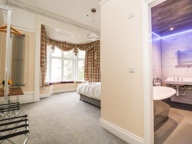 A bedroom with a bed and plaid curtains by a bay window next to a bathroom with a bathtub at The Lloyd George in Bontnewydd Gwynedd