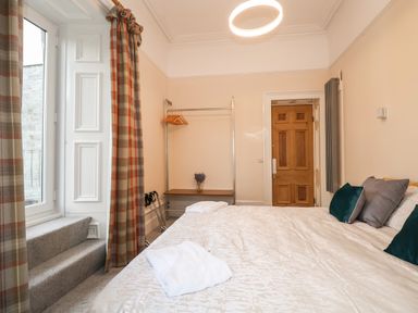 A bedroom with a bed with pillows and a folded towel a wooden door a clothes rack with hangers and a window with plaid curtains at The Lloyd George in Bontnewydd Gwynedd