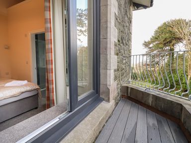 A bedroom with a bed and open door leading to a balcony with railing and stone wall at The Lloyd George in Bontnewydd Gwynedd