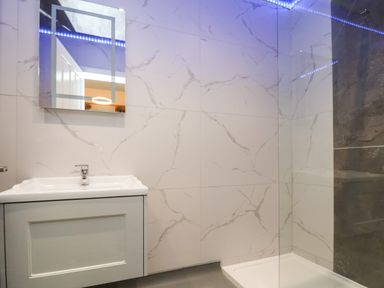 A bathroom with a sink, mirror, and shower area with marble tiled walls at The Lloyd George in Bontnewydd Gwynedd