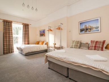 A bedroom with two beds, pillows, a window with plaid curtains, framed pictures on the walls, and a clothing rack at The Lloyd George in Bontnewydd, Gwynedd