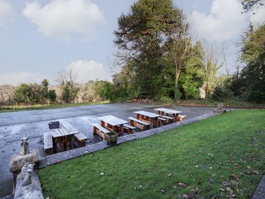 An outdoor area with wooden picnic tables and benches surrounded by trees and grass at The Lloyd George in Bontnewydd Gwynedd