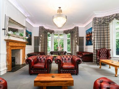 A living room with leather armchairs wooden tables a fireplace and large windows with curtains at The Lloyd George in Bontnewydd Gwynedd