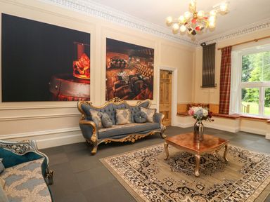 A living room with two sofas a coffee table with flowers on a rug and large paintings on the wall at The Lloyd George in Bontnewydd Gwynedd