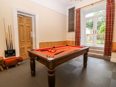 A game room with a pool table and cues near a wooden door and windows with curtains at The Lloyd George in Bontnewydd Gwynedd