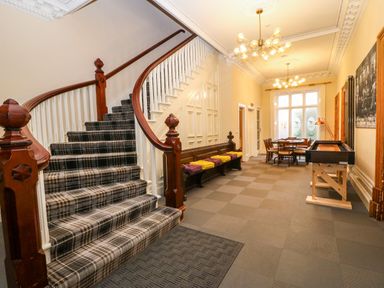A hallway with a plaid carpeted staircase wooden bench with cushions a table and chairs and pendant lights at The Lloyd George in Bontnewydd Gwynedd