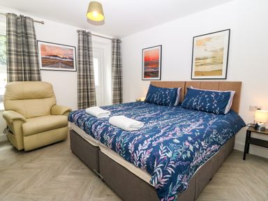 A bedroom with a double bed blue floral bedding a beige armchair and framed pictures on the wall at The Lloyd George in Bontnewydd Gwynedd