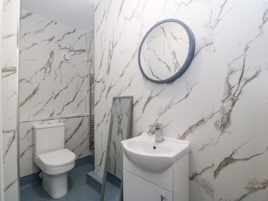 A bathroom with a toilet sink and round mirror on marble patterned walls at The Lloyd George in Bontnewydd Gwynedd
