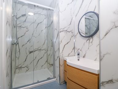 A bathroom with a glass shower enclosure a wooden vanity with a sink and a round mirror at The Lloyd George in Bontnewydd Gwynedd