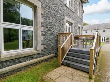 A stone building with wooden stairs leading to a small deck with a table and chairs at The Lloyd George in Bontnewydd Gwynedd