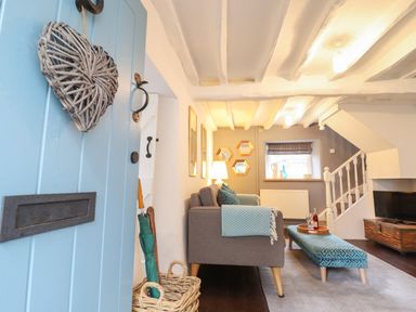 A living room with a blue door wicker heart hanging sofa and ottoman near staircase and TV at 3 Ivy Court in Dolgellau