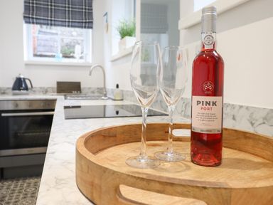 A kitchen with a wooden tray holding a bottle of pink port and two wine glasses at 3 Ivy Court in Dolgellau