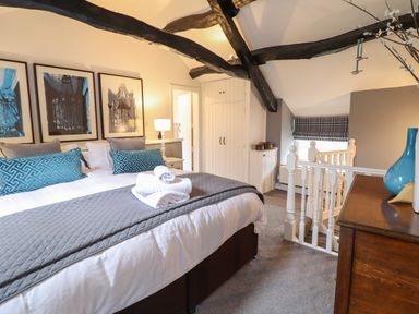 A bedroom with a bed towels pillows wall art wooden beams and a staircase at 3 Ivy Court in Dolgellau