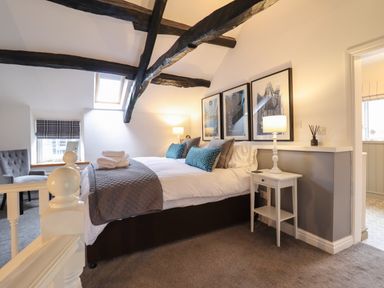 A bedroom with a bed pillows lamps framed pictures and exposed wooden beams at 3 Ivy Court in Dolgellau