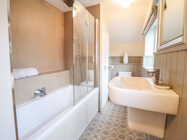 A bathroom with a bathtub shower combination a sink a toilet and patterned floor tiles at 3 Ivy Court in Dolgellau