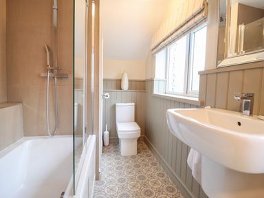 A bathroom with a bathtub shower combination toilet sink window and patterned floor at 3 Ivy Court in Dolgellau